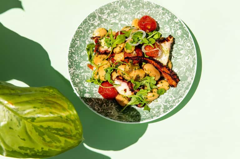 Grilled seafood and mushroom dish on decorative green plate with fresh greens