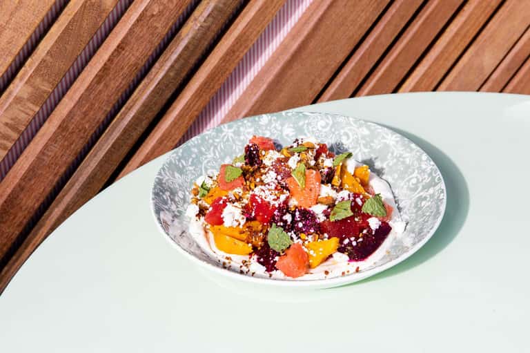 Colorful beet and vegetable salad with feta cheese and fresh herbs served on white plate