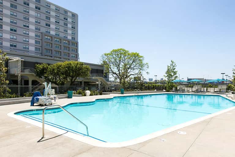 Bright blue rectangular swimming pool with lounge chairs and surrounding resort buildings on a sunny day