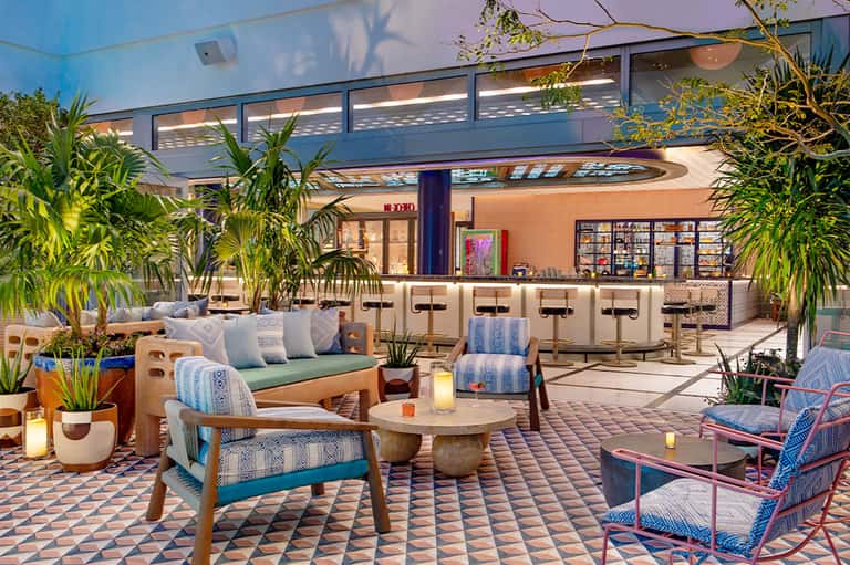Modern resort lounge with blue-upholstered seating, potted plants, and geometric floor tiles