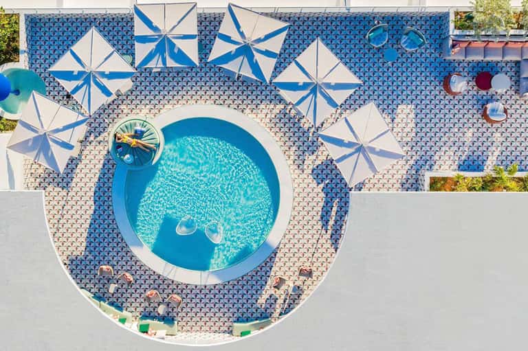 Aerial view of circular swimming pool surrounded by striped umbrellas and patterned deck