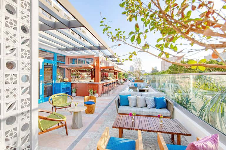 Colorful rooftop bar and lounge area with blue and orange accents, seating, and city skyline views.