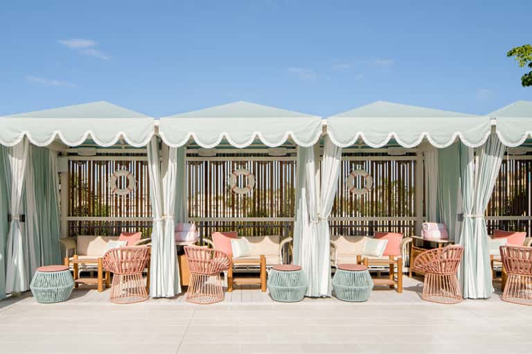 Luxury resort cabanas with white peaked canopies, coral chairs, and ocean view