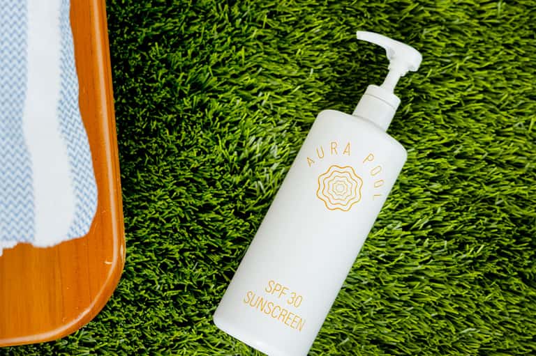 Aura Pool SPF 30 sunscreen bottle with pump dispenser on artificial green grass surface