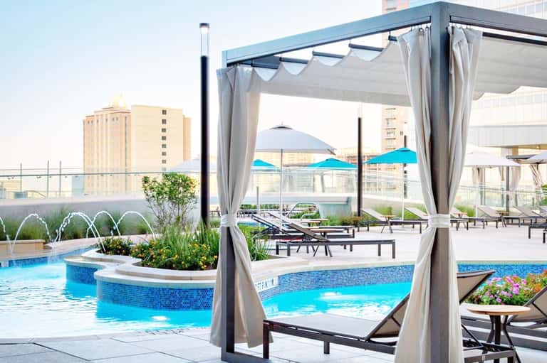 Rooftop pool area with gray cabanas, blue water, and city skyline views