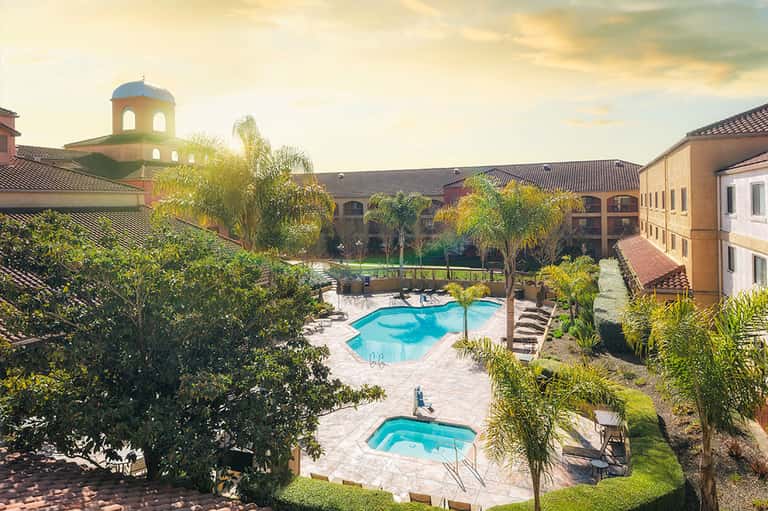 Luxury resort courtyard with two pools, palm trees, Spanish architecture, and manicured grounds
