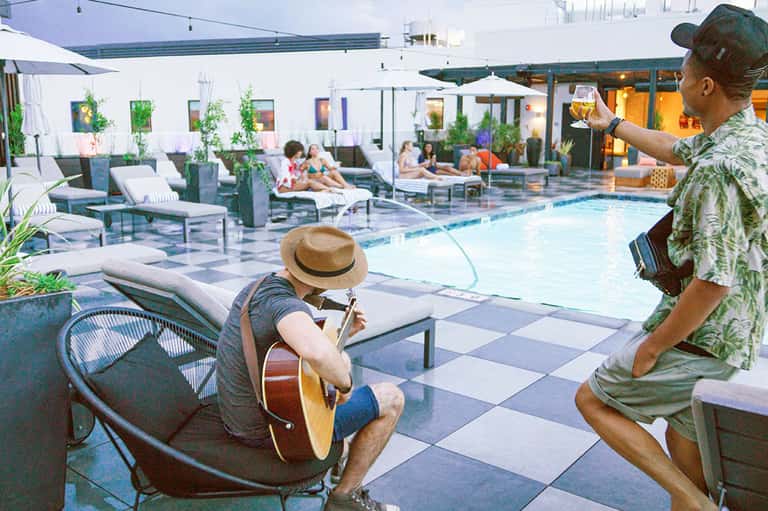 Rooftop pool deck with guests relaxing, live musician playing guitar, and evening ambiance