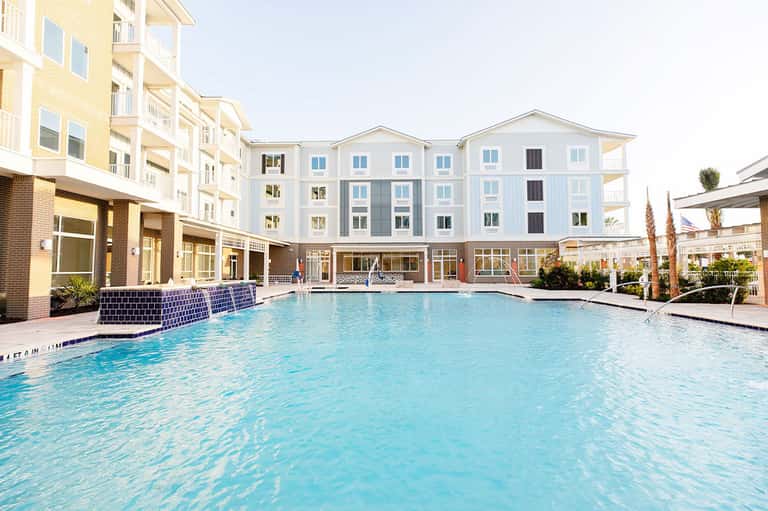 Resort courtyard with large swimming pool surrounded by multi-story hotel buildings with brick and white facades