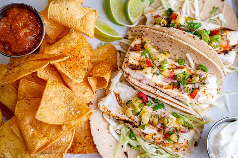 Fish tacos with lime, cilantro garnish and tortilla chips with salsa on white plate