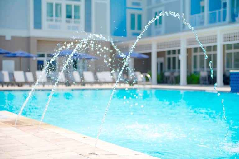 Resort swimming pool with water fountains and modern white building architecture in background