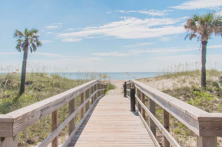 Wooden boardwalk leading to a sandy beach with palm trees and ocean view