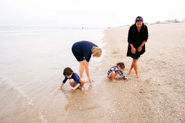 Family playing in shallow ocean water on sandy beach with adults supervising