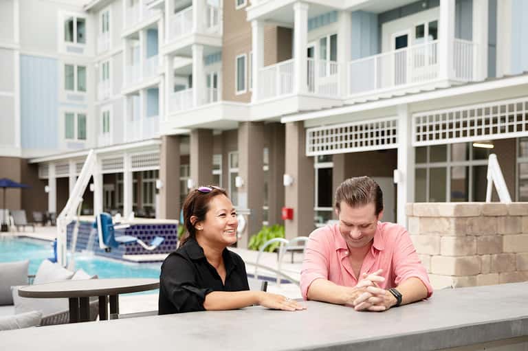 Two hotel staff members smiling at outdoor poolside counter with modern residential buildings in background