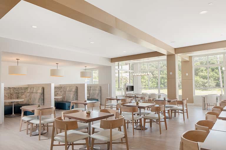 Modern hotel lounge with exposed wood beams, pendant lighting, booth seating, and large windows