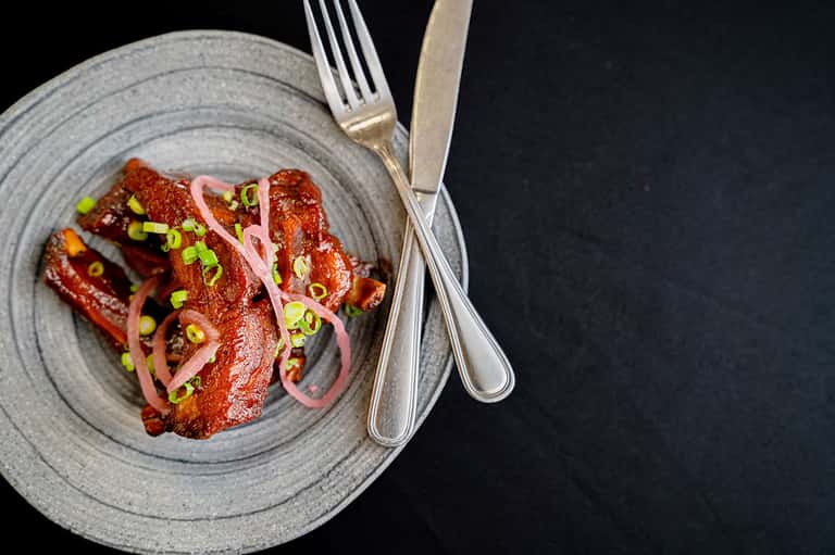 Gourmet plated dish of seared red meat with pickled vegetables and microgreens on gray ceramic plate