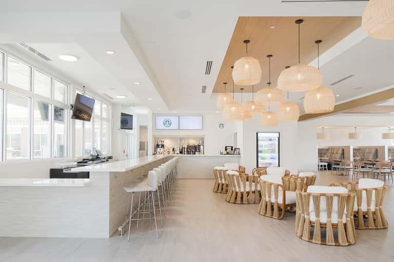 Modern hotel café interior with wooden ceiling, pendant lights, and woven chairs