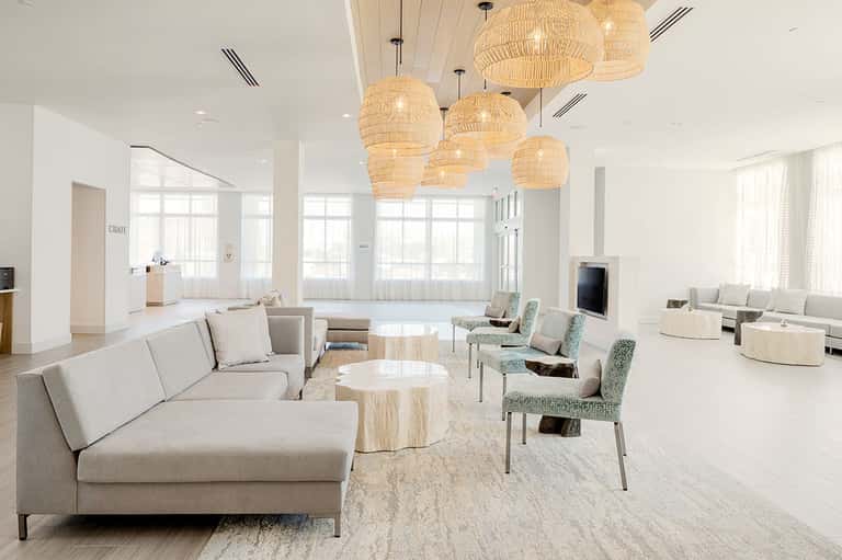Bright modern lobby with beige sectional sofas, woven pendant lights, and natural lighting from large windows