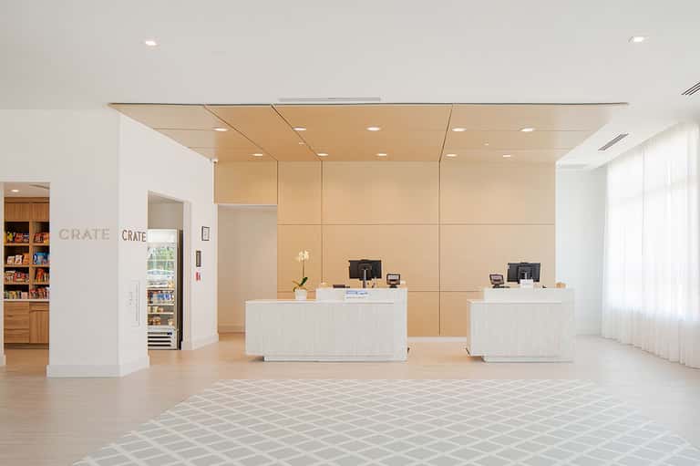 Bright hotel lobby with dual reception desks, wooden wall panels, and minimalist design