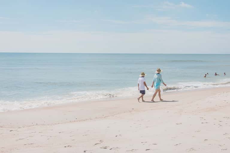 Two children walking along sandy beach toward clear turquoise ocean water on sunny day