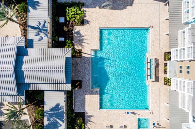 Aerial view of rectangular swimming pool surrounded by sand and residential buildings