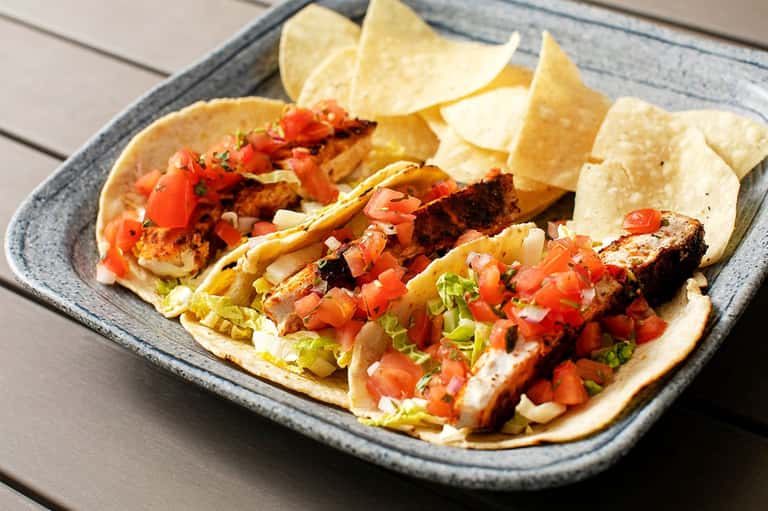 Grilled fish tacos with fresh salsa, lettuce, and tortillas served with tortilla chips on a gray plate