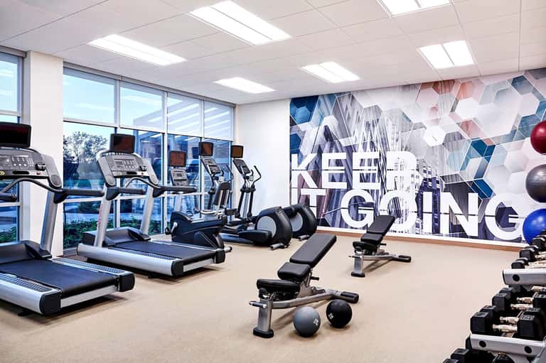 Modern fitness center with cardio equipment, dumbbells, motivational wall art, and floor-to-ceiling windows