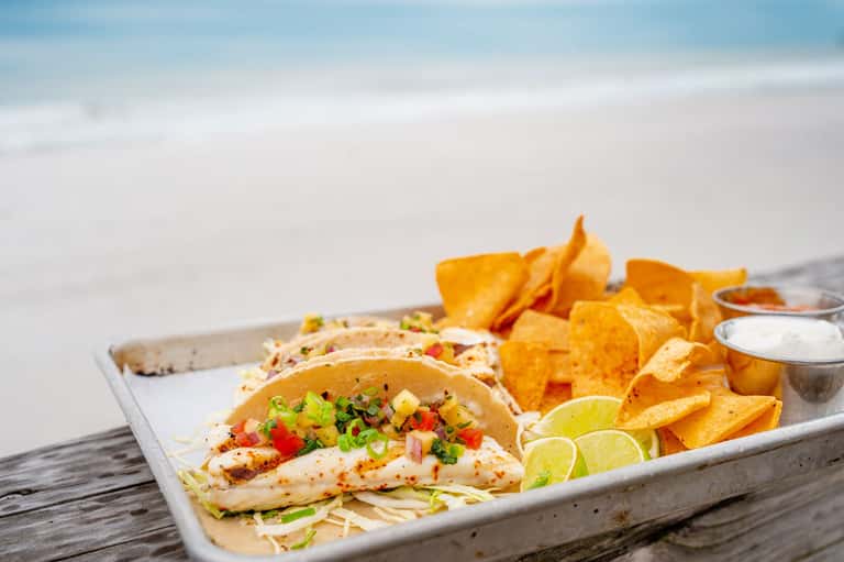 Grilled fish tacos with crispy chips and lime on white plate served beachside