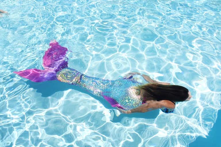 Woman swimming underwater in crystal-clear turquoise pool wearing colorful mermaid tail fin