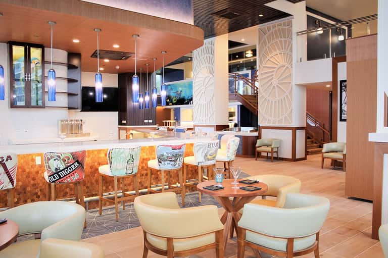 Modern hotel bar and lounge with orange accents, pendant lights, and colorful upholstered seating
