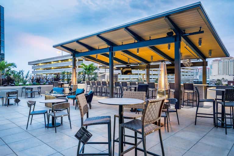 Rooftop dining area with wooden pergola, blue accent chairs, and city skyline views during daytime
