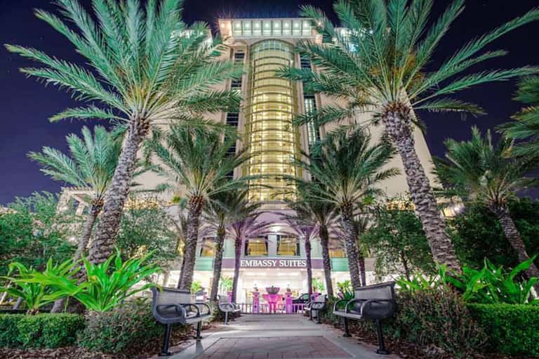 Embassy Suites hotel entrance at night, illuminated with palm trees lining the courtyard