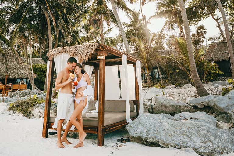 Couple relaxing in beachfront cabana with palm trees and sandy beach