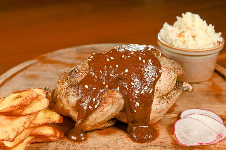 Grilled meat with sesame seeds, fries, and side dishes on a wooden serving board
