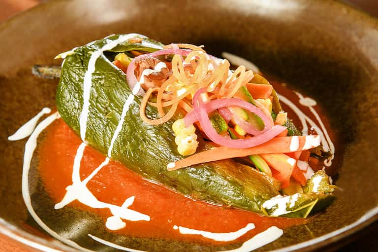 Gourmet appetizer with green leaf wrap, pickled ginger, and sriracha on ceramic plate