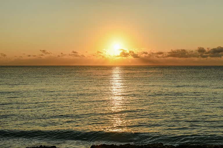 Golden sunset over calm ocean waters with clouds and sun reflecting on the sea