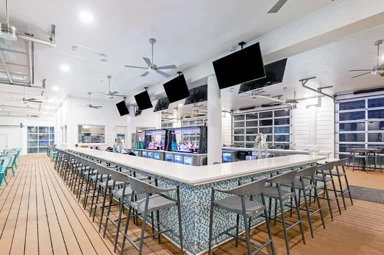 Modern resort bar with white counter, bar seating, multiple TV screens, and ocean view doors