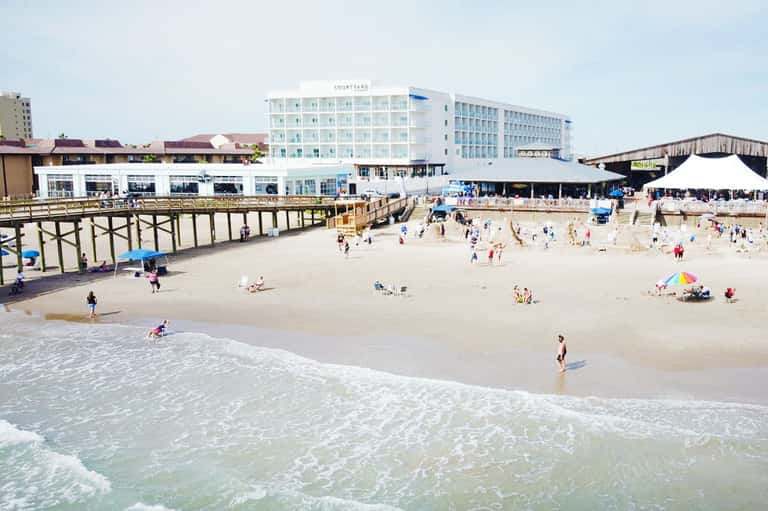Sandy beach with Courtyard hotel, pier, and crowds of beachgoers on sunny day