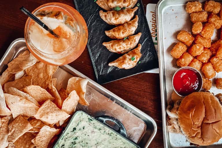 Appetizer spread featuring chips with dip, dumplings, fried appetizers, and cocktail on wooden table