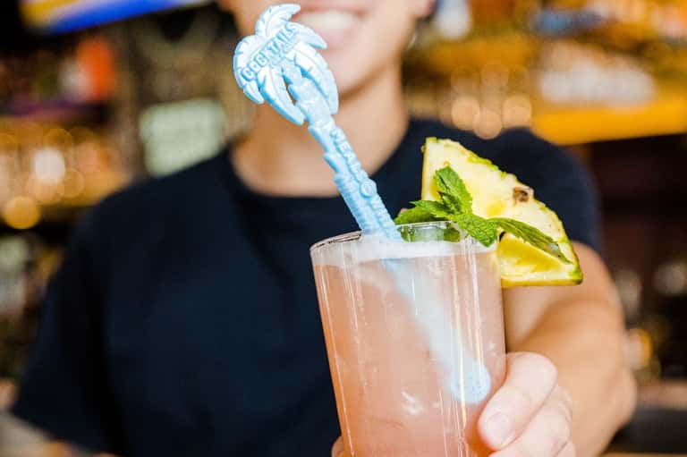 Tropical cocktail with blue decorative stirrer, pineapple wedge, and mint garnish in a clear glass