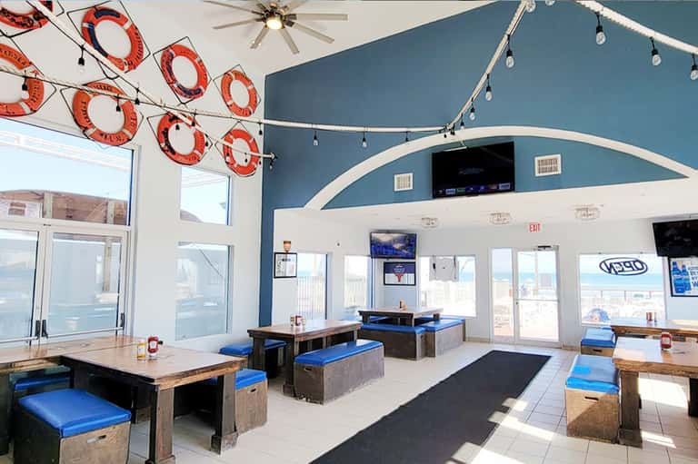 Beachfront restaurant interior with blue curved walls, decorative life rings, and ocean views