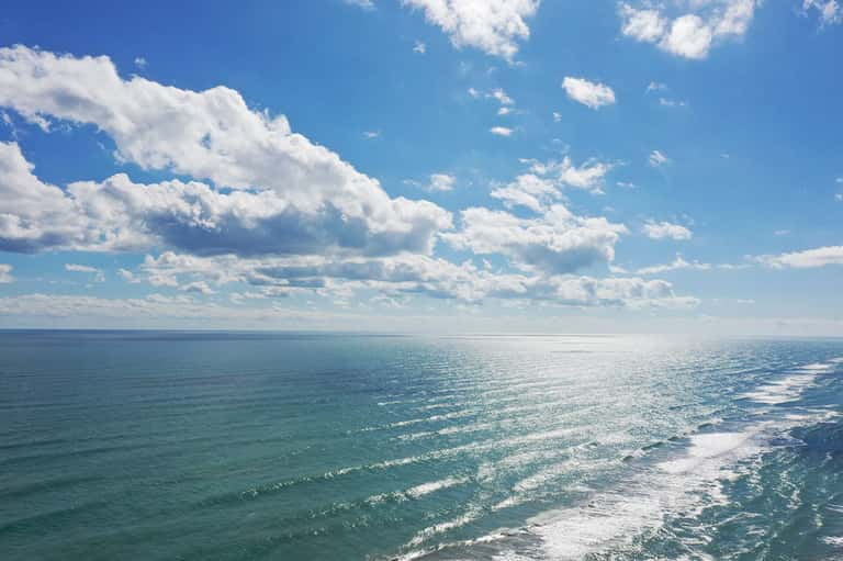 Scenic ocean view with turquoise waves and white clouds under blue sky
