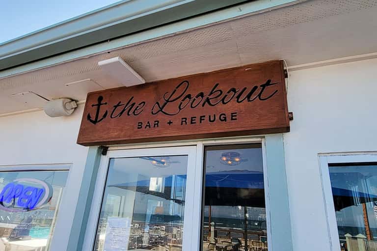 Wooden 'The Lookout Bar + Refuge' sign on beachfront establishment entrance