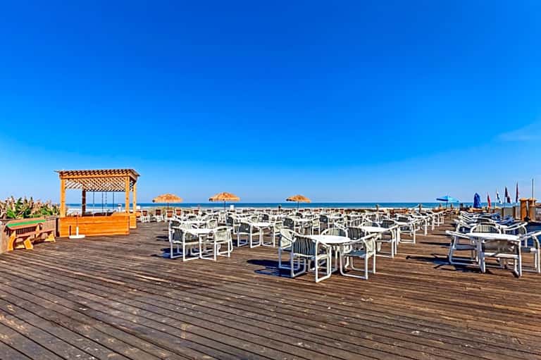 Wooden boardwalk with white chairs and thatched umbrellas overlooking beach and ocean