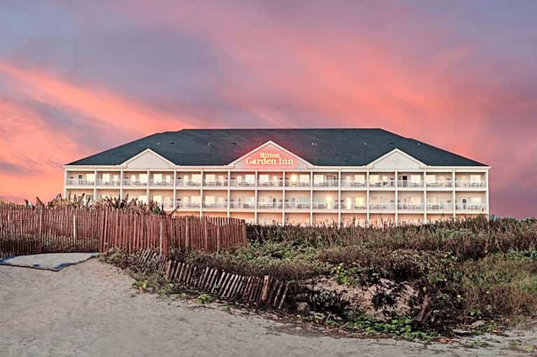 Hilton Garden Inn beachfront hotel at sunset with dune fencing and dramatic pink sky