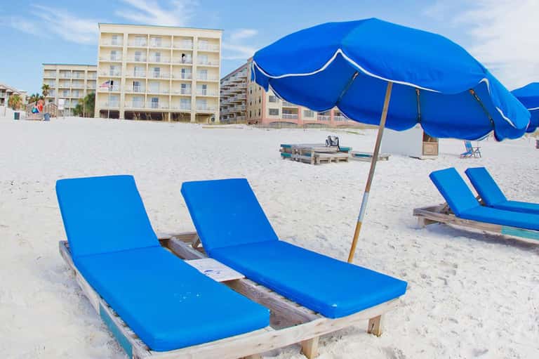Sandy beach with blue lounge chairs, umbrellas, and beachfront hotel buildings