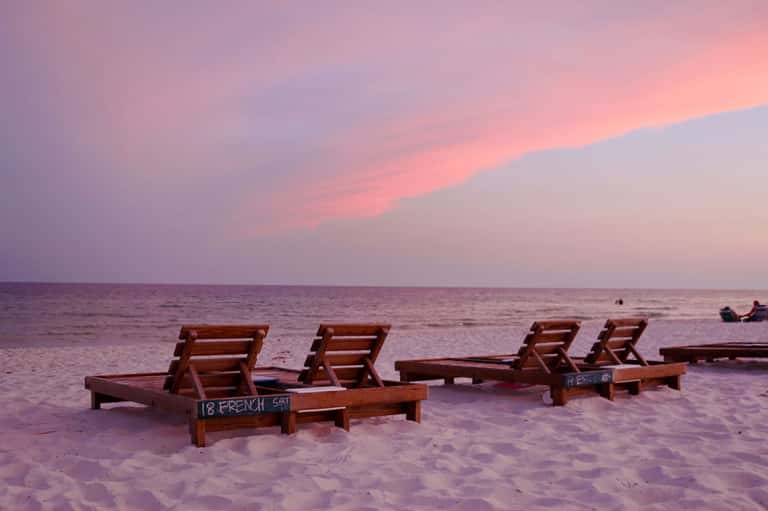 Wooden beach loungers on sand at sunset with ocean horizon and pink sky