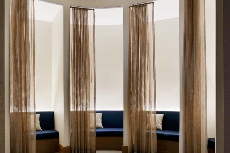 Modern spa relaxation room with sheer curtains separating private seating alcoves with navy cushions