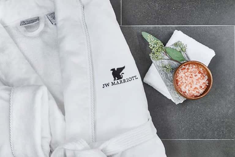 JW Marriott white bathrobe with logo displayed next to spa salt and decorative greenery
