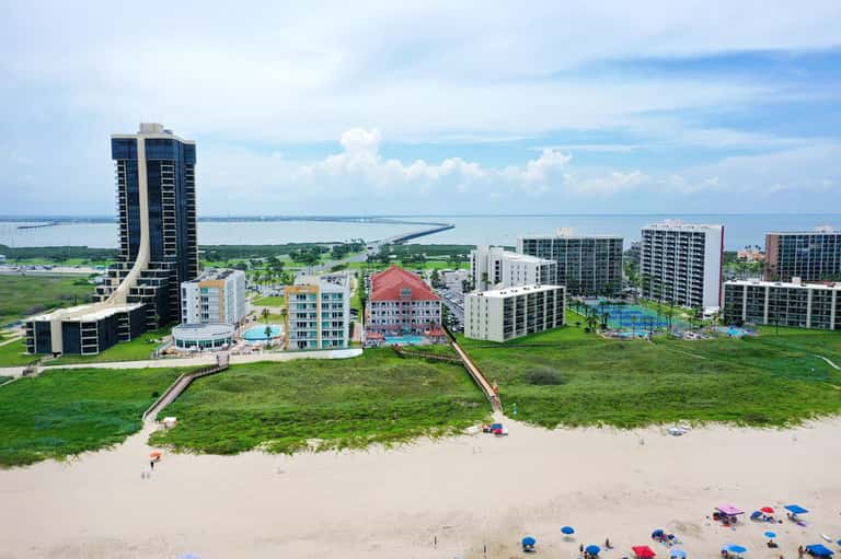 Aerial view of beachfront resort with high-rise hotel tower, multiple buildings, and beach with umbrellas