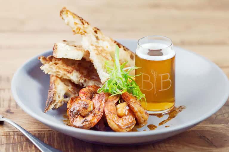 Grilled shrimp and toast appetizers on a plate with a beer glass on wooden table